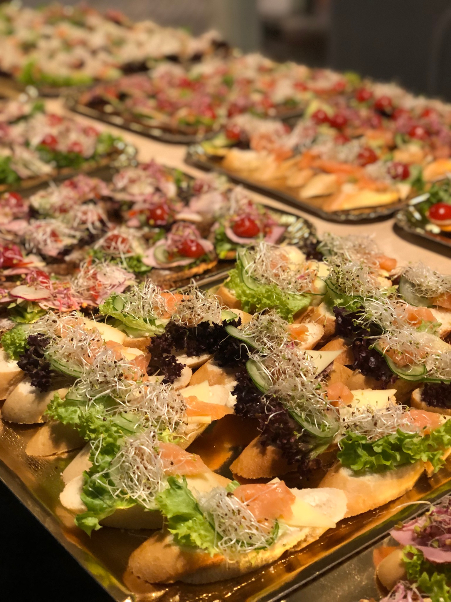 Apetyczne kanapeczki na złotych tacach, bogato udekorowane świeżymi warzywami, łososiem i kiełkami, gotowe do serwowania na przyjęciu.