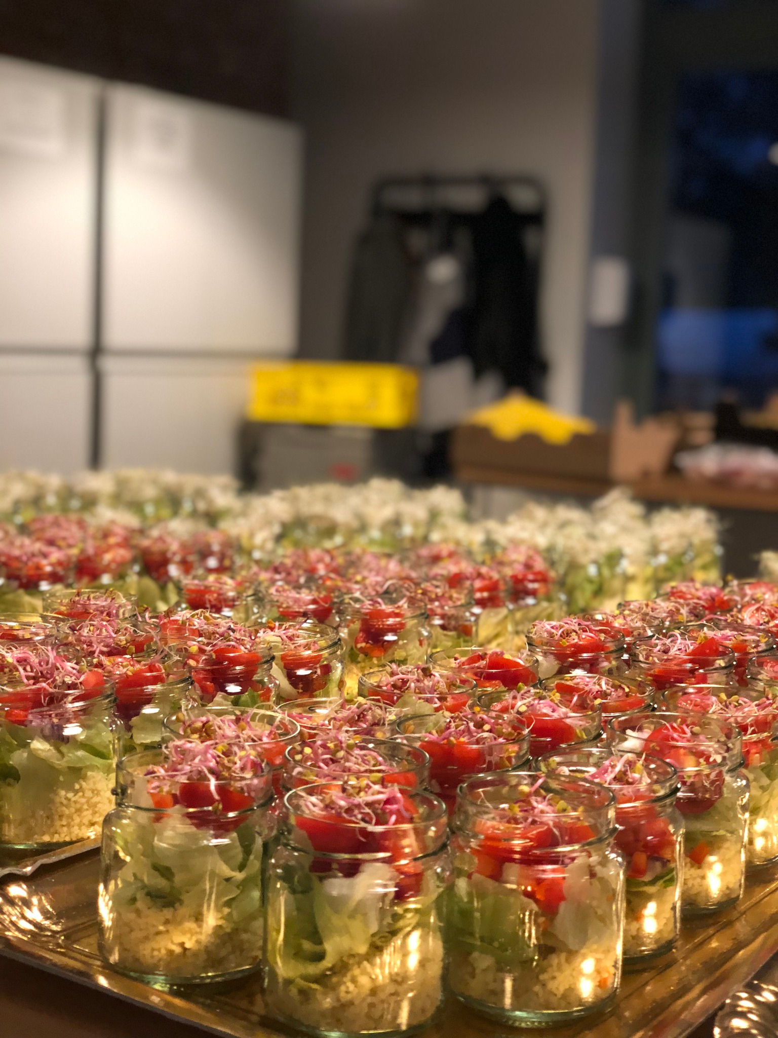 Rząd słoików z sałatkami na cateringowej tacy, widoczne warstwy kaszy, sałaty, pomidorów i kiełków. Przygotowane na przyjęcie.