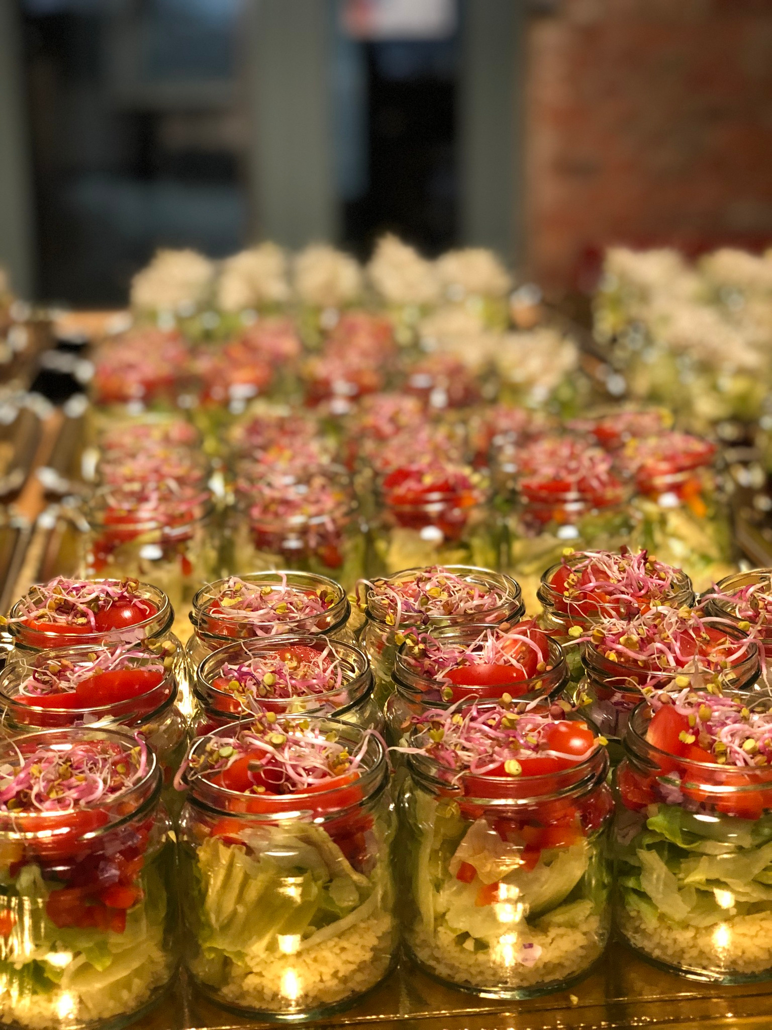 Rząd słoików z warstwową sałatką: kasza, sałata, pomidory i kiełki. Catering dietetyczny, zdrowe przekąski w szklanych pojemnikach, gotowe do spożycia.