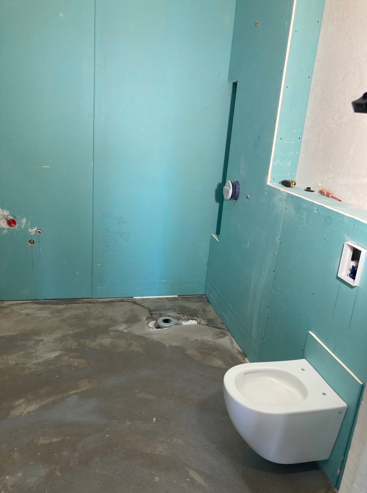 Montaż płyty KG w łazience, widoczna podtynkowa instalacja WC, surowy beton na podłodze i ściany przygotowane do dalszych prac wykończeniowych.