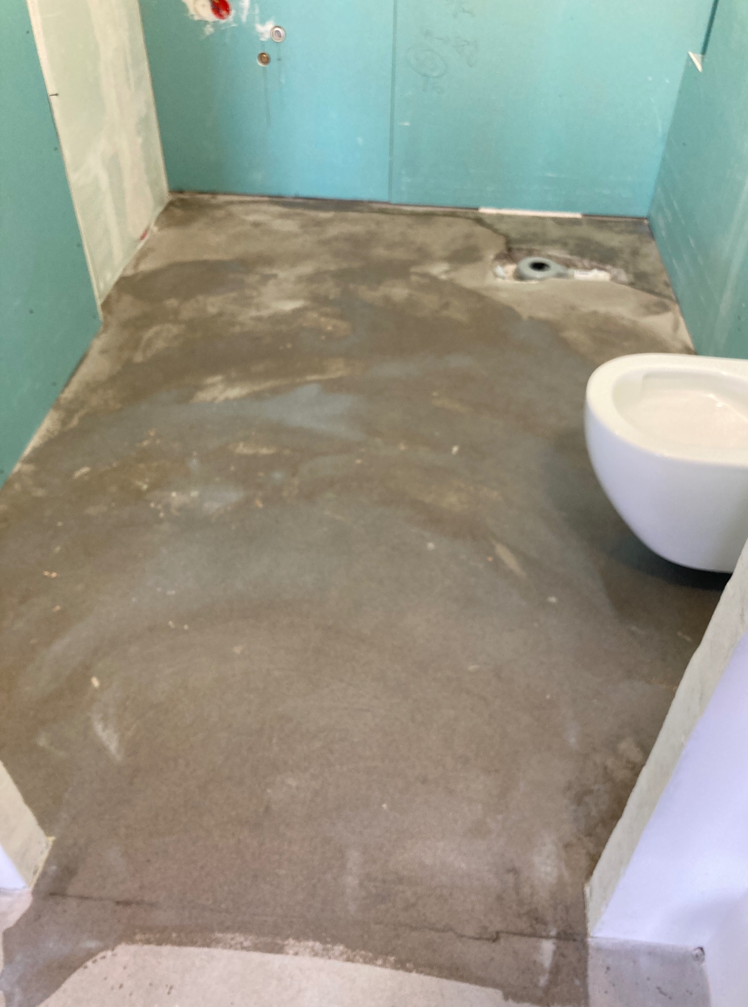 Przygotowanie podłoża w łazience: wylewka samopoziomująca, ściany z płyt karton-gips, odpływ liniowy. Częściowo widoczna toaleta.