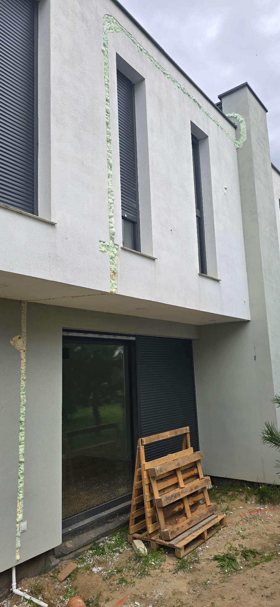 Szczeliny okienne wypełnione pianką montażową na elewacji budynku w Zgierzu, widok z zewnątrz. Na dole paleta drewniana.