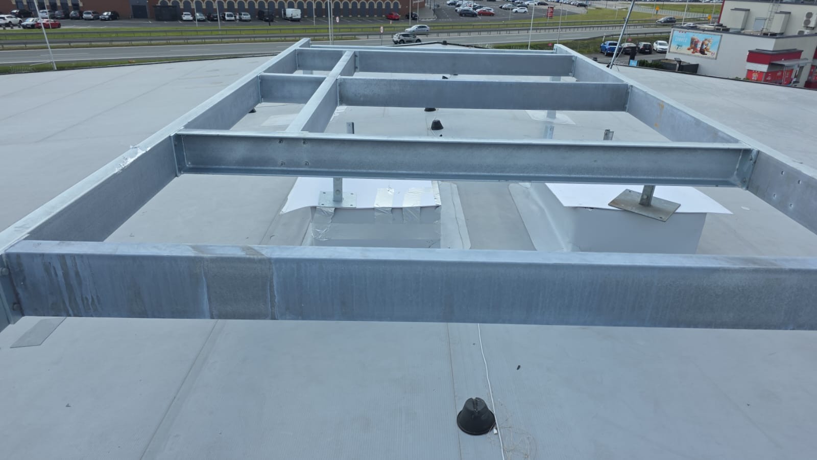 Metalowa konstrukcja wsporcza na dachu budynku, prawdopodobnie pod klimatyzację lub wentylację, z widocznymi elementami montażowymi i otoczeniem miejskim.