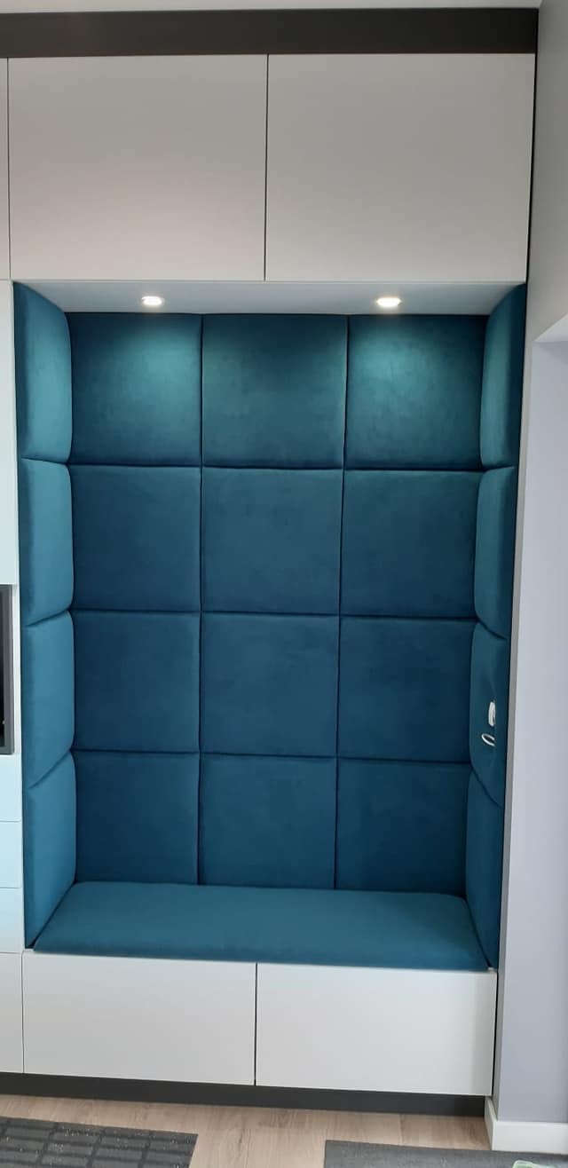 Narożnik tapicerowany wnękowy w odcieniach błękitu, zabudowany szafkami w kolorze białym. Oświetlenie punktowe. Całość tworzy przytulny kącik.