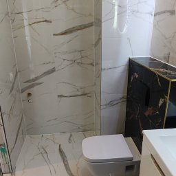 WM House - Elegancka łazienka z marmurowymi płytkami, podwieszaną toaletą i szafką umywalkową w kolorze białym, oświetlona ledowym lustrem.