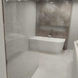 WM House - Elegancka łazienka z kabiną prysznicową ze szkła i wolnostojącą wanną na tle ściany z płytek imitujących marmur, oświetlona punktowo.