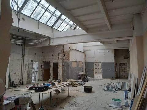 Przestronne wnętrze w trakcie demontażu: odsłonięte ściany, widoczne instalacje, narzędzia na stole, sufit z oknami dachowymi. Etap przygotowawczy do dalszych prac.
