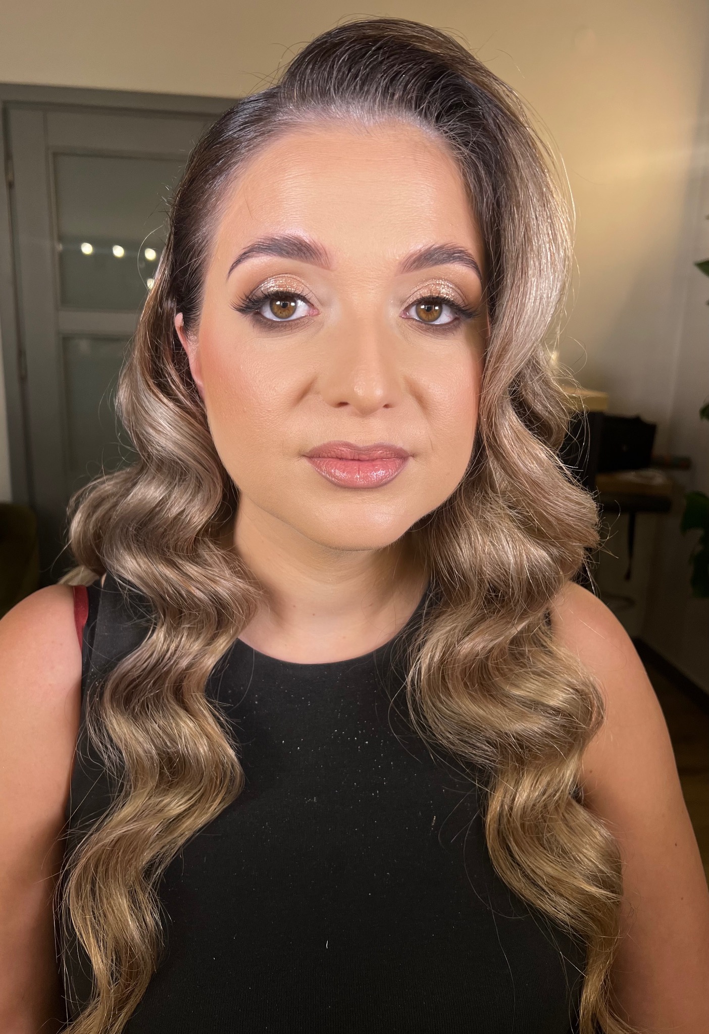 Portret kobiety z profesjonalnym makijażem oczu w odcieniach złota i brązu, z błyszczącymi ustami i ułożonymi falami włosów w kolorze blond.