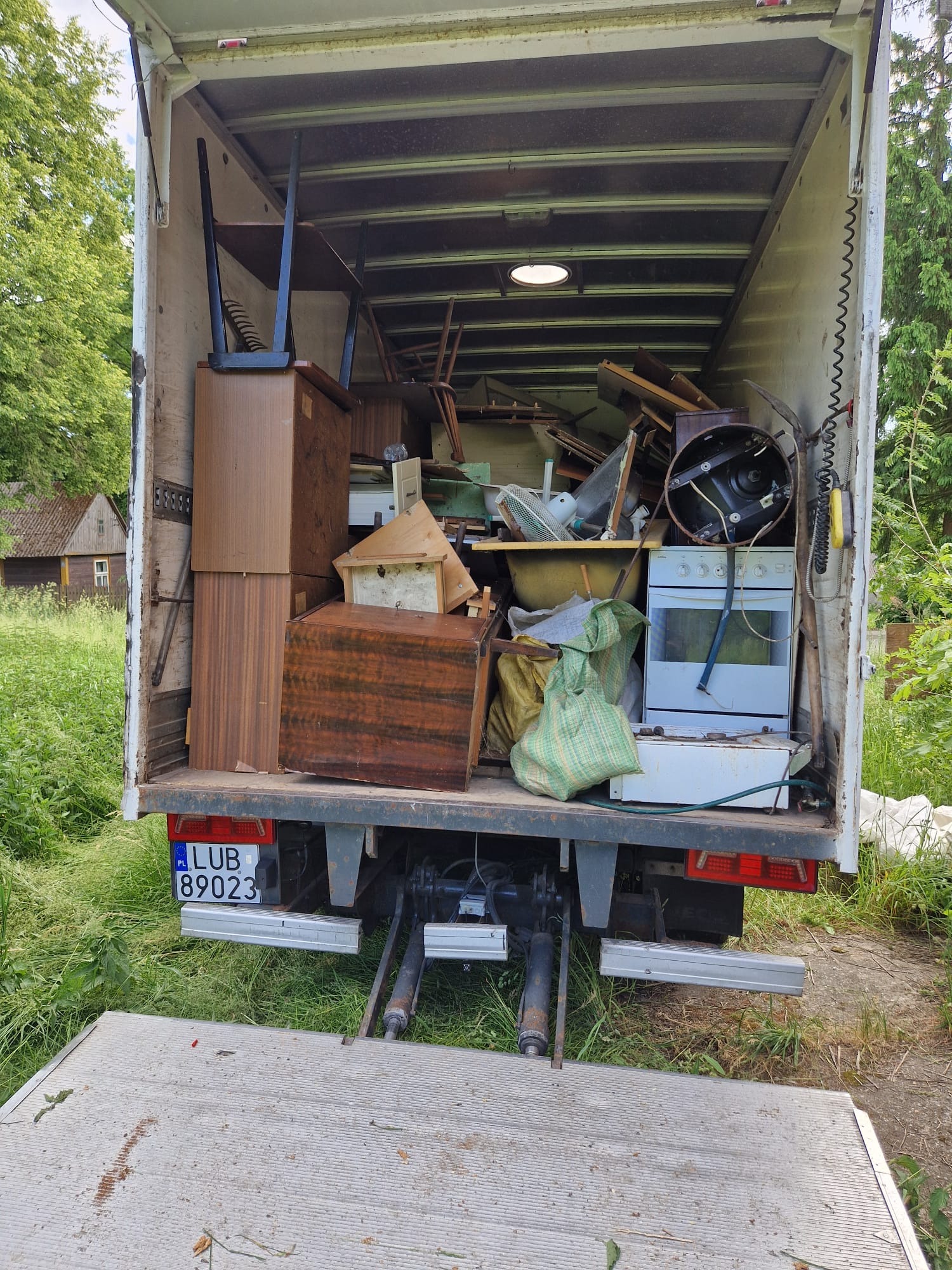 Wnętrze białej furgonetki wypełnionej meblami, sprzętem AGD i różnymi przedmiotami podczas opróżniania mieszkania. Widoczny numer rejestracyjny pojazdu.
