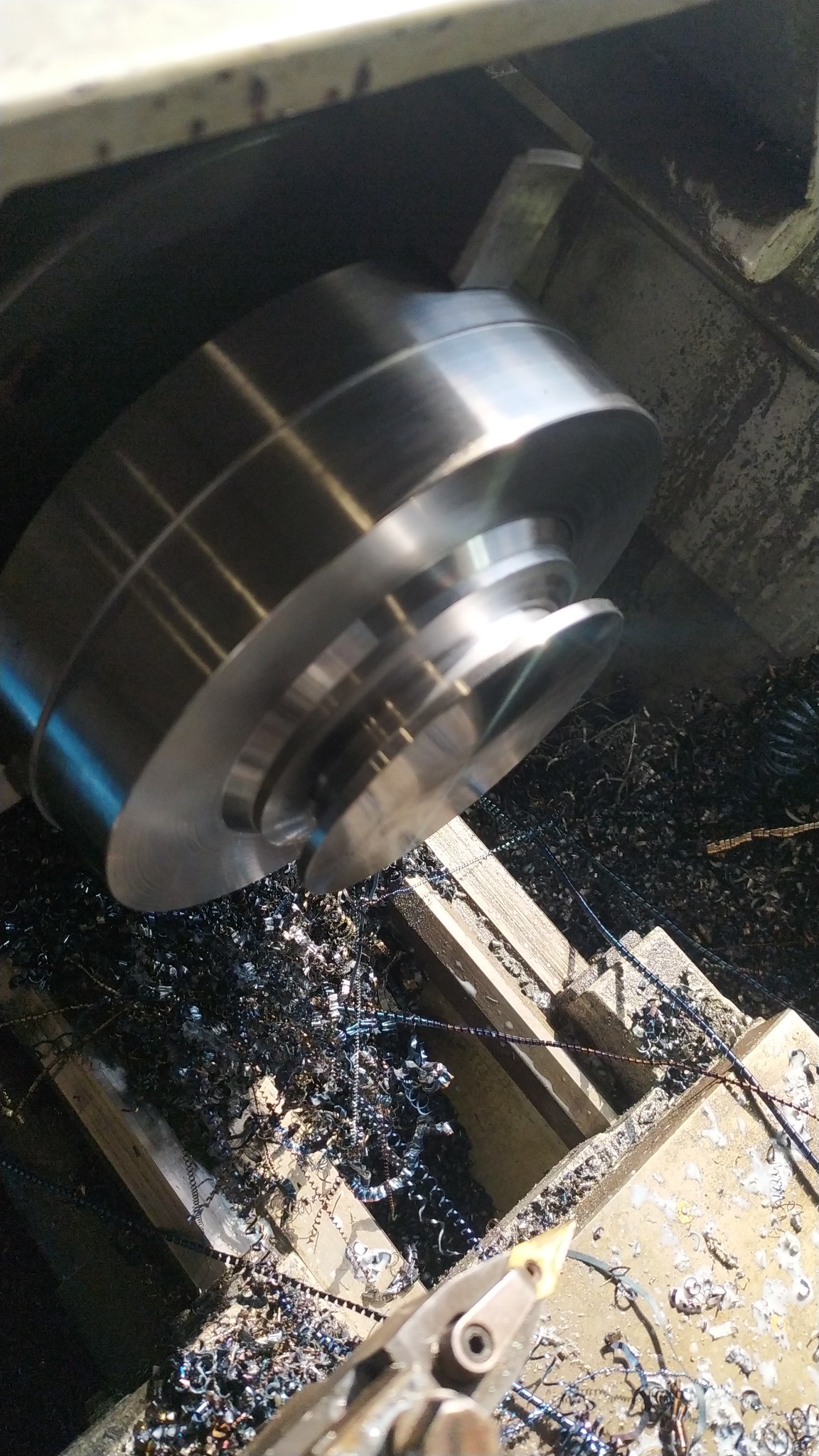 Metalowy element obrabiany w tokarce, otoczony wiórami. Widoczne ślady obróbki skrawaniem i narzędzie. Ujęcie z góry, podkreślające detale procesu.