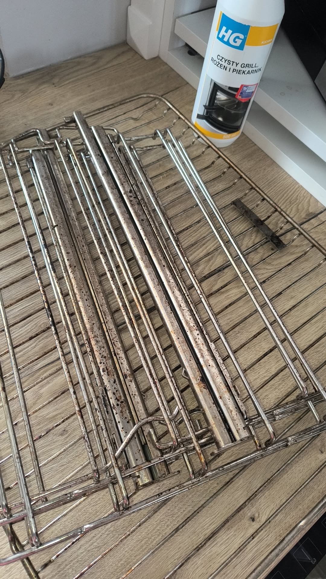 Zanieczyszczony ruszt z piekarnika, widoczny środek czyszczący HG. Detal brudnego rusztu przed czyszczeniem, z osadami i przypaleniami na metalowych prętach.