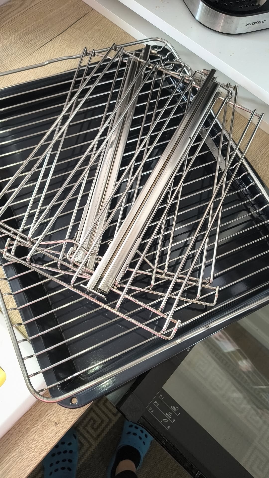 Wyjęta z piekarnika blacha i ruszt, przygotowane do umycia. Widoczne ślady użytkowania. Ujęcie z góry, fragment blatu i piekarnika.