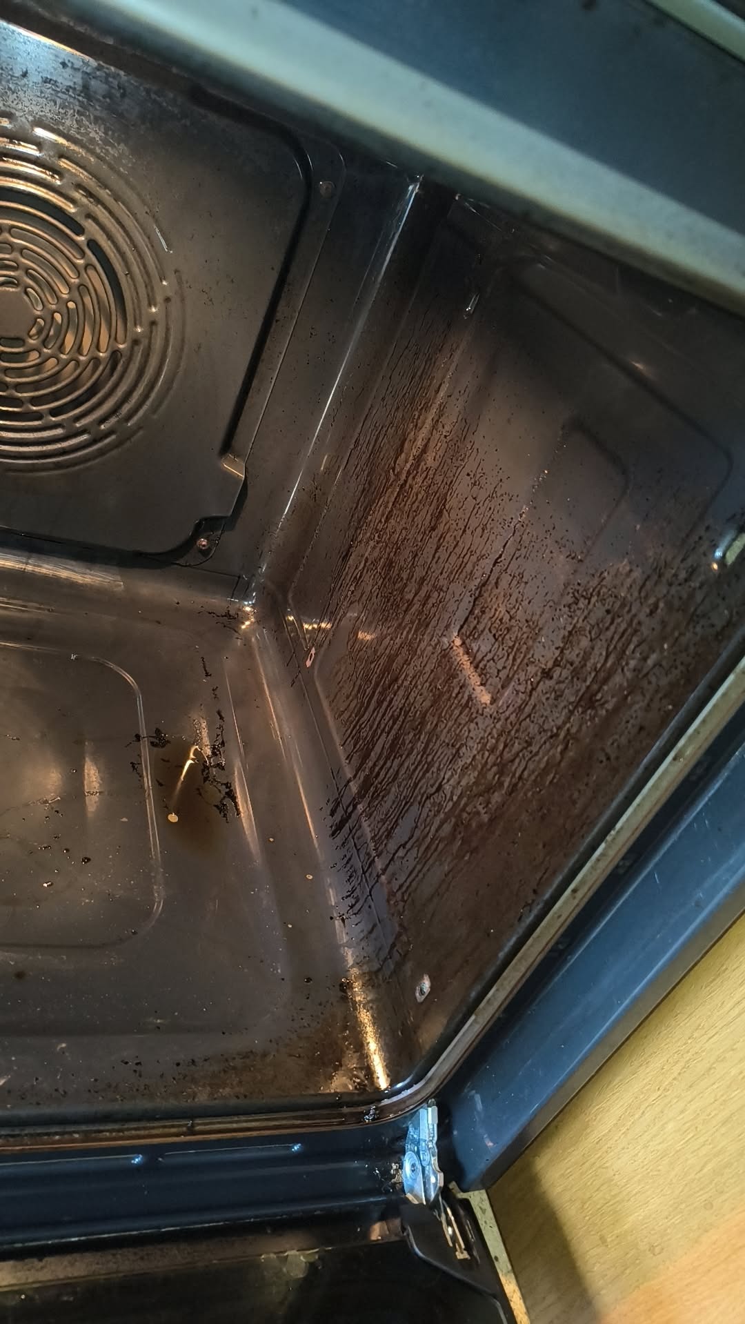 Wnętrze brudnego piekarnika z zaschniętym tłuszczem na ściankach i dnie, widok z góry, przed czyszczeniem. Metalowe elementy i kratka wentylacyjna.