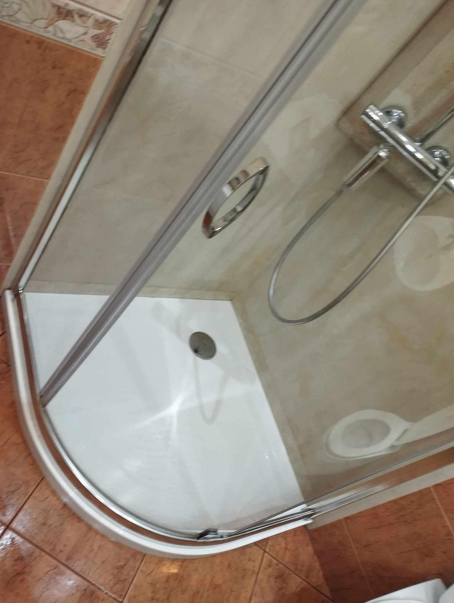 Wyczyszczona kabina prysznicowa z chromowaną armaturą i odpływem, widok z góry, po sprzątaniu. Jasne płytki na ścianach i podłodze.