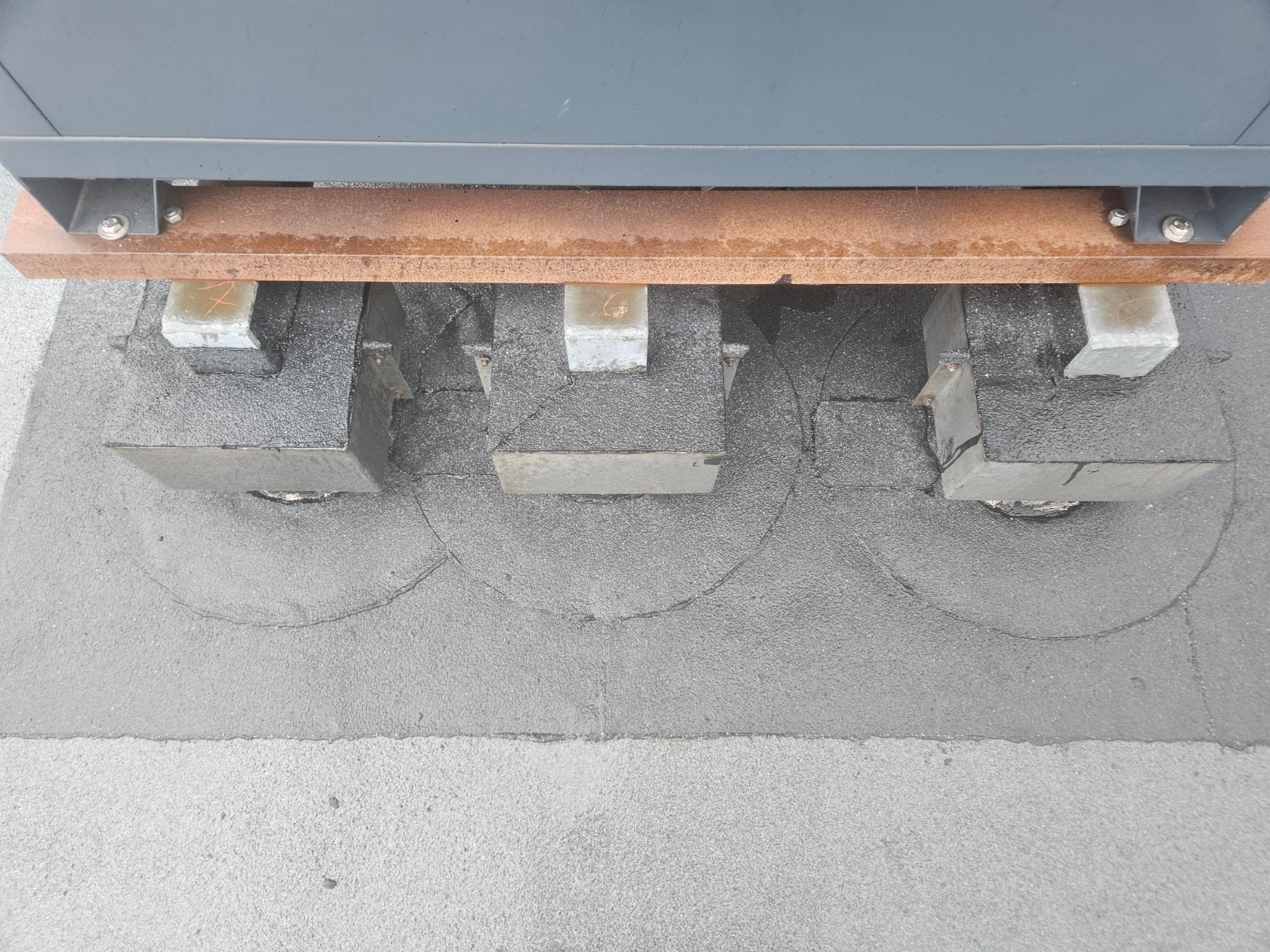 Szczegółowe ujęcie izolacji dachu płaskiego z betonowymi wspornikami pod konstrukcją, widoczne ślady po okręgach, świeżo położona papa.