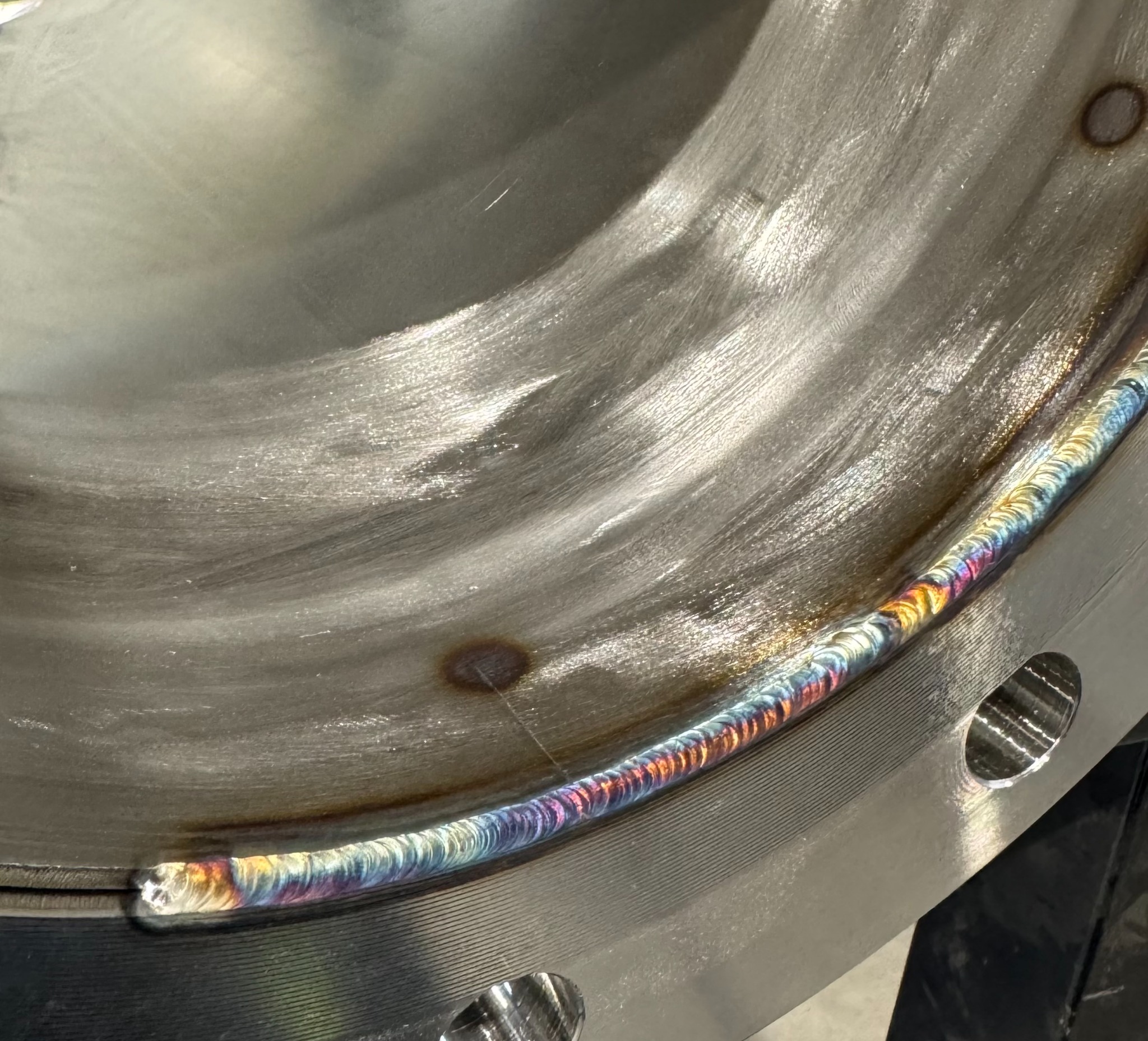 Precyzyjny spaw na metalowej rurze, widoczne tęczowe przebarwienia termiczne, świadczące o wysokiej jakości wykonania. Detal z bliska, widoczne ślady obróbki.