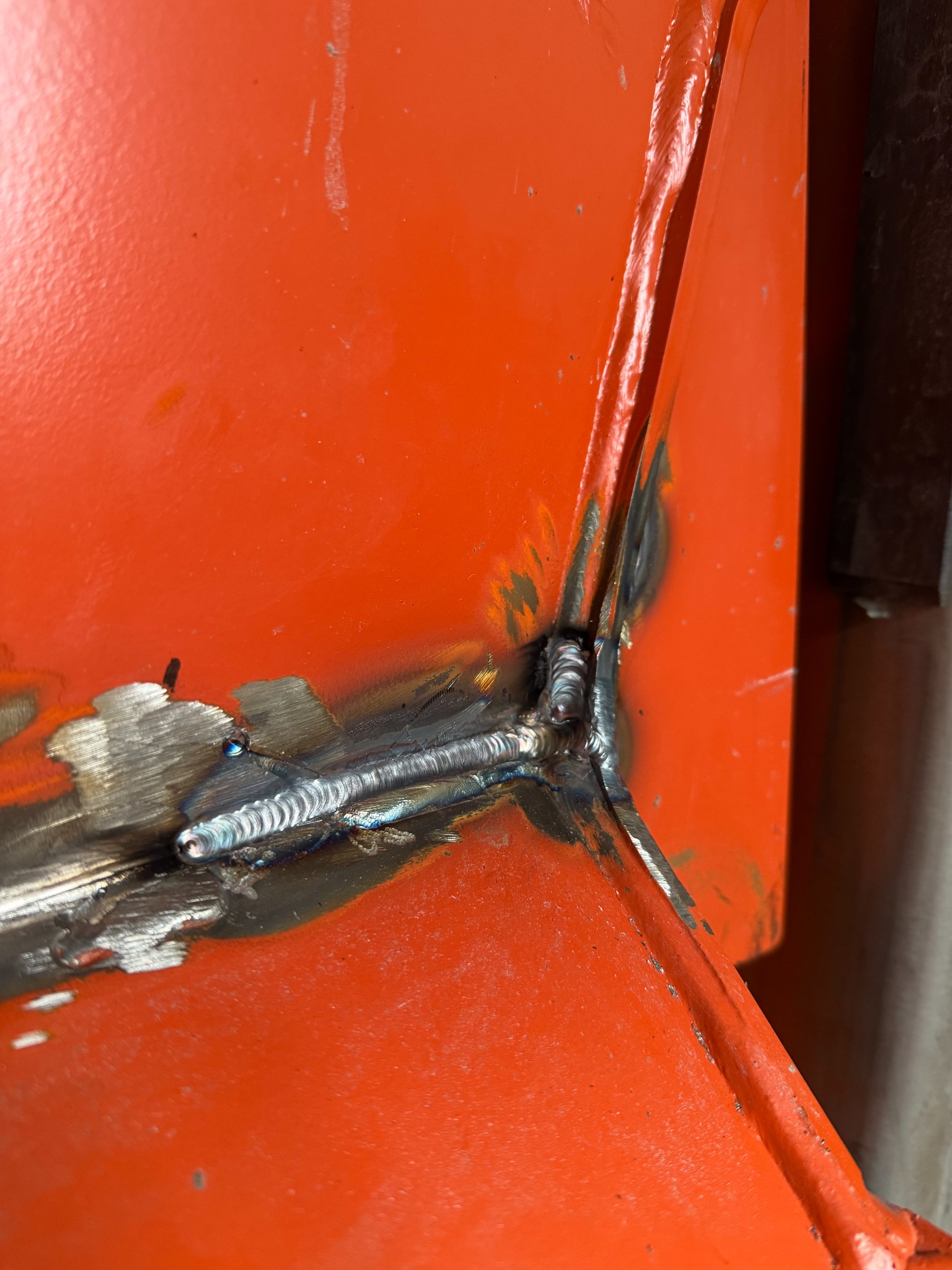 Pomarańczowy element konstrukcyjny po spawaniu. Widoczne spoiwo i ślady obróbki. Detal z bliska ukazuje precyzję wykonania spoiny.