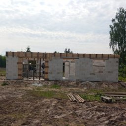 Grzegorz Mołas - Wznoszenie ścian z betonu komórkowego domu jednorodzinnego. Widoczne drewniane nadproża okienne i drzwiowe. Na pierwszym planie sterta drewna budowlanego.