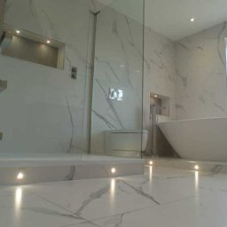 FI-WIT INTERIORS S.C. - Elegancka łazienka z marmurowymi płytkami, przeszkloną kabiną prysznicową i wolnostojącą wanną pod oknem. Podświetlenie LED w podłodze. Nowoczesny design.