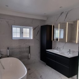 FI-WIT INTERIORS S.C. - Elegancka łazienka po remoncie: marmurowe płytki, czarne szafki z podwójną umywalką, wanna wolnostojąca i kabina prysznicowa ze szklanymi drzwiami.