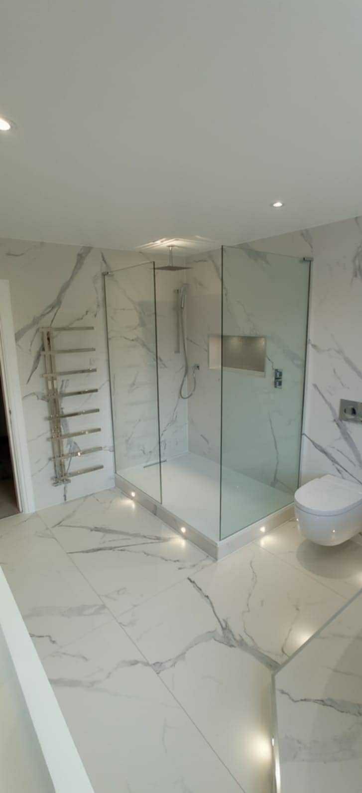 Elegancka łazienka z kabiną prysznicową typu walk-in, płytkami imitującymi marmur oraz oświetleniem punktowym w podłodze i grzejnikiem drabinkowym.