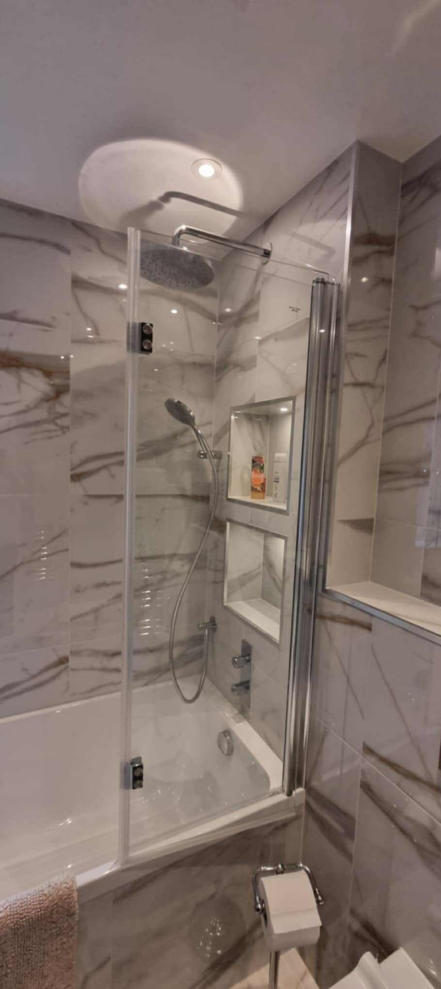 Elegancka łazienka w odcieniach bieli i szarości z marmurowymi płytkami. Kabina prysznicowa z deszczownicą i wnękami na kosmetyki. Nowoczesny design.