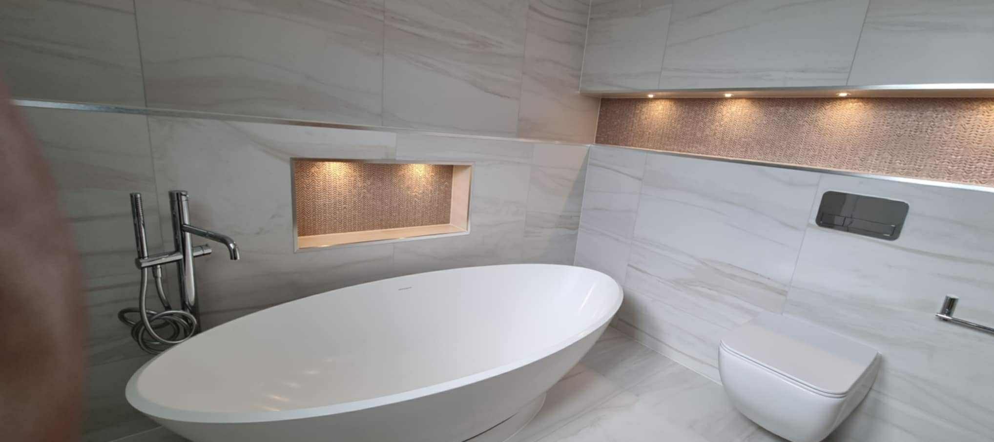 Nowoczesna łazienka z wolnostojącą wanną, marmurowymi płytkami i podświetlanymi wnękami. Armatura chromowana, toaleta podwieszana. Aranżacja po remoncie.