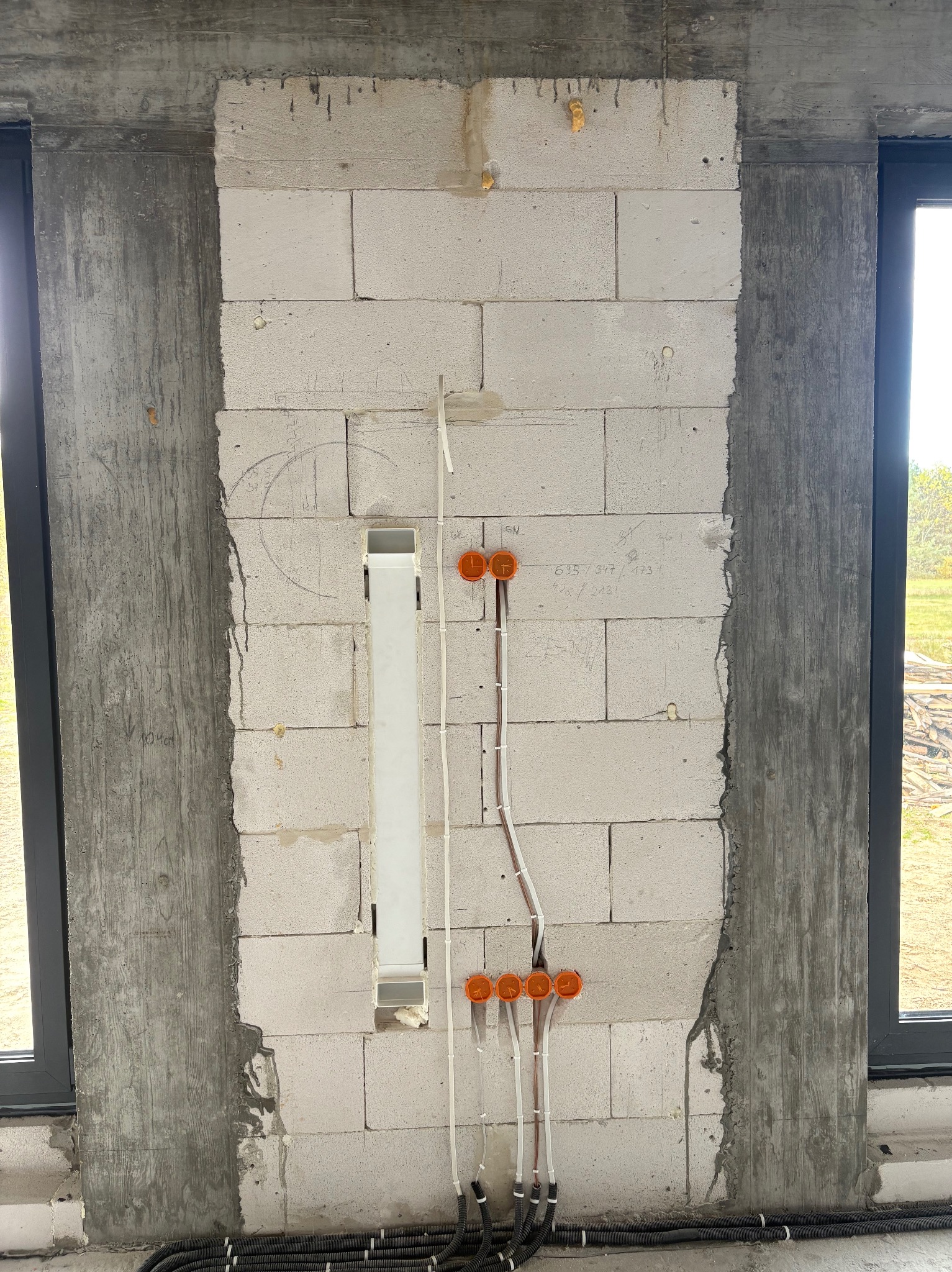 Ściana z betonu komórkowego z widocznymi przewodami elektrycznymi w peszlach i puszkami instalacyjnymi. Widoczne okno i fragment instalacji podtynkowej.