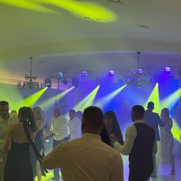 Holiday zespół muzyczny weselny obsługa wesel eventów - Parkiet taneczny wypełniony tańczącymi osobami, oświetlony dynamicznymi światłami scenicznymi w odcieniach żółci i fioletu, tworzącymi żywą atmosferę imprezy.