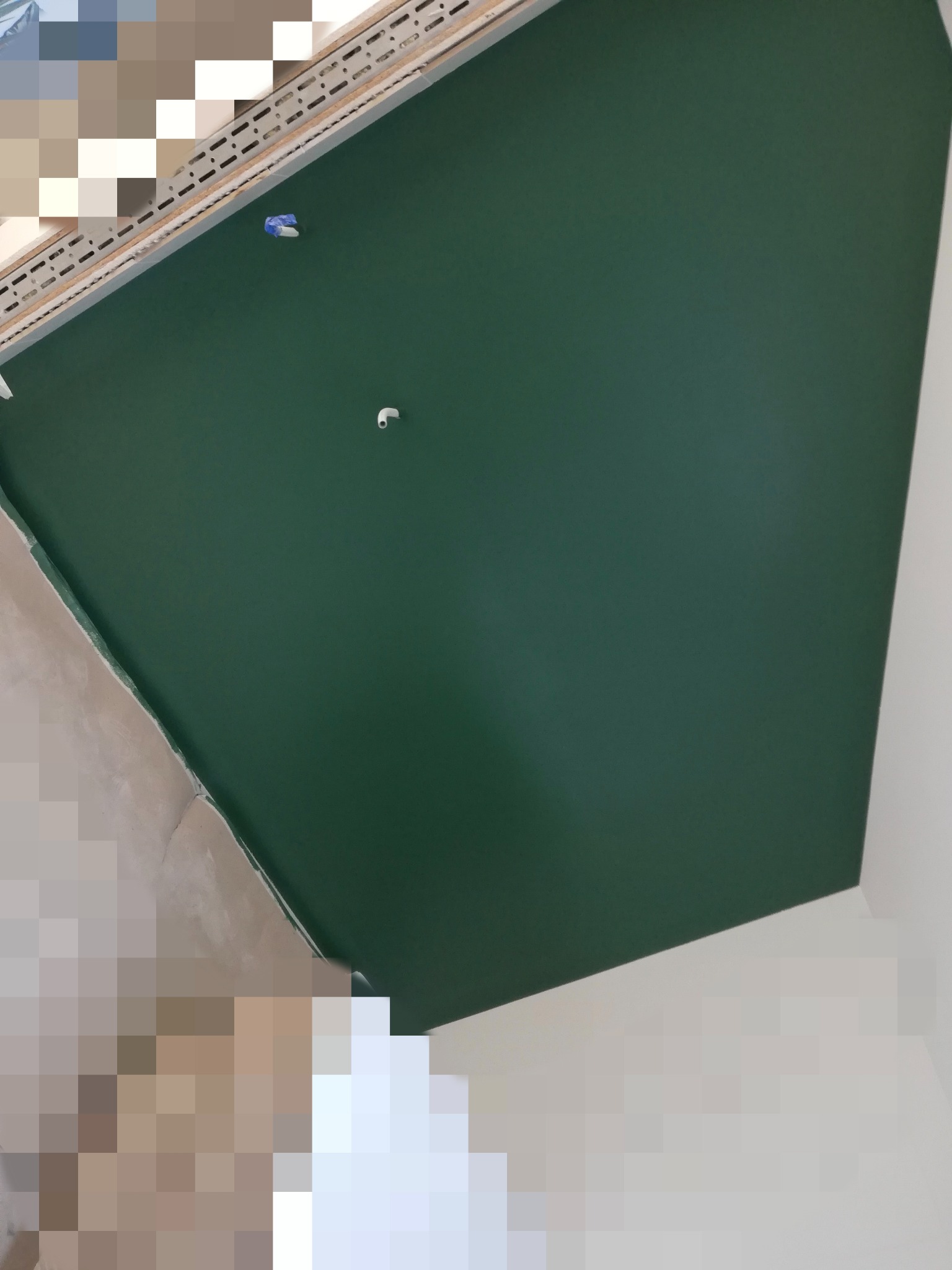 Pomalowany na zielono sufit z wystającym elementem instalacji. Widoczny fragment ściany w neutralnym odcieniu. Ujęcie z dołu, ukośne.