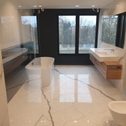 Kierownik robót instalacji sanitarnych - wykonawstwo, nadzór, projekt - Nowoczesna łazienka z marmurową podłogą, wolnostojącą wanną i wiszącą szafką z umywalką. Duże okno z widokiem na drzewa. Minimalistyczny design.