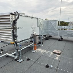 Kierownik robót instalacji sanitarnych - wykonawstwo, nadzór, projekt - Szara instalacja wentylacyjna Ventus Compact na dachu budynku z widocznymi elementami mocującymi i zabezpieczeniami odgromowymi.
