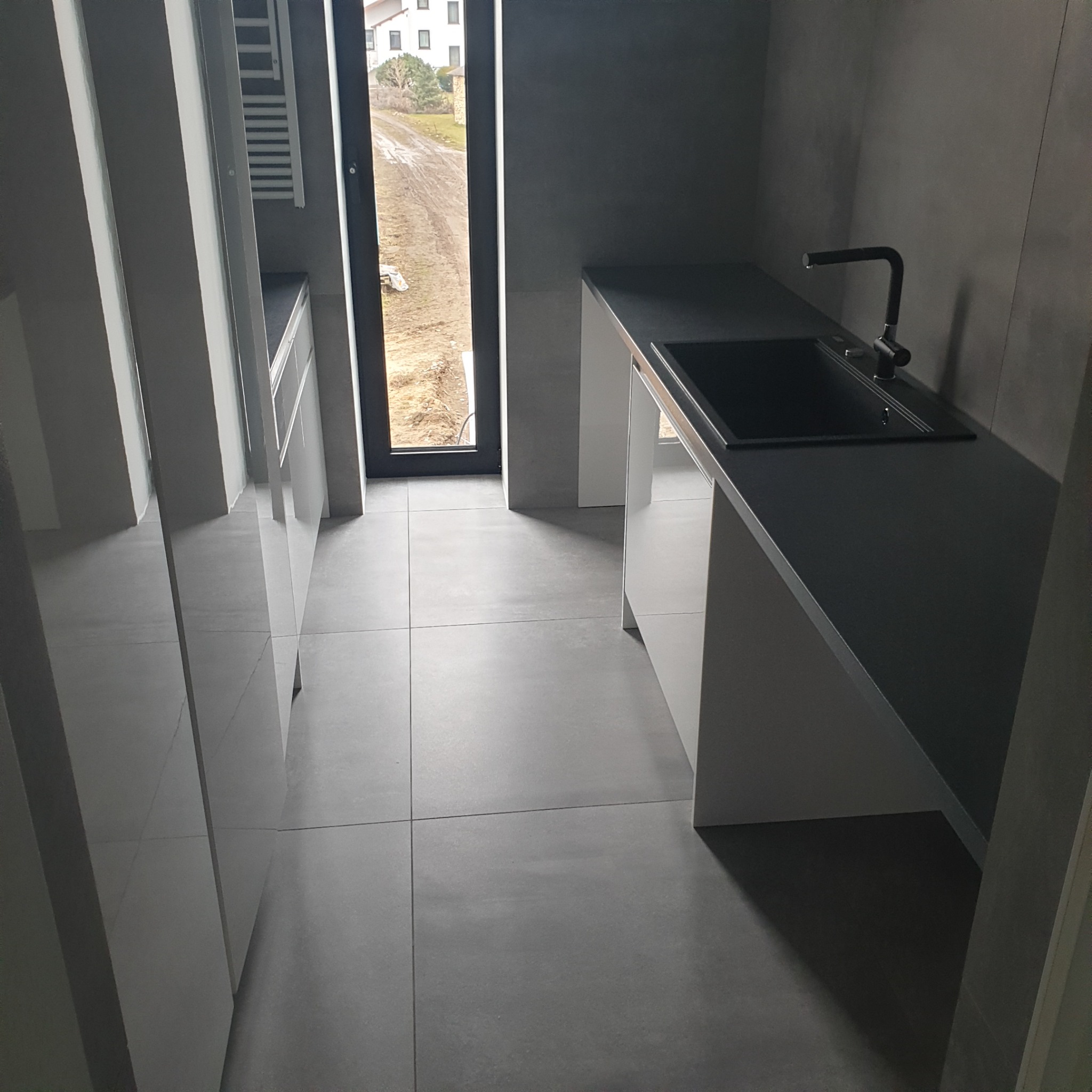 Nowoczesna, szara łazienka z czarną armaturą i dużym oknem z widokiem na zewnątrz. Minimalistyczny design, płytki podłogowe w odcieniach szarości.