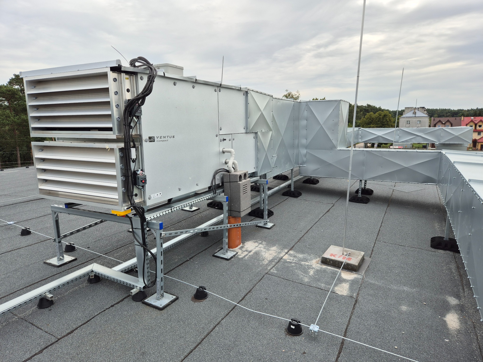Szara instalacja wentylacyjna Ventus Compact na dachu budynku z widocznymi elementami mocującymi i zabezpieczeniami odgromowymi.