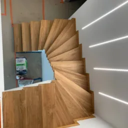 Wewnętrzne, dębowe schody kręcone z podświetleniem LED wzdłuż ściany. Widok z góry ukazuje detale wykończenia i układ stopni.