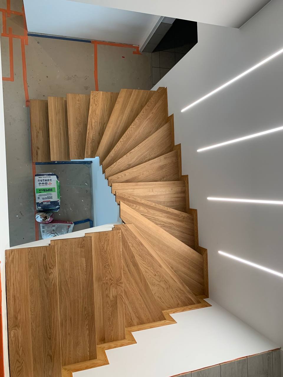 Wewnętrzne, dębowe schody kręcone z podświetleniem LED wzdłuż ściany. Widok z góry ukazuje detale wykończenia i układ stopni.