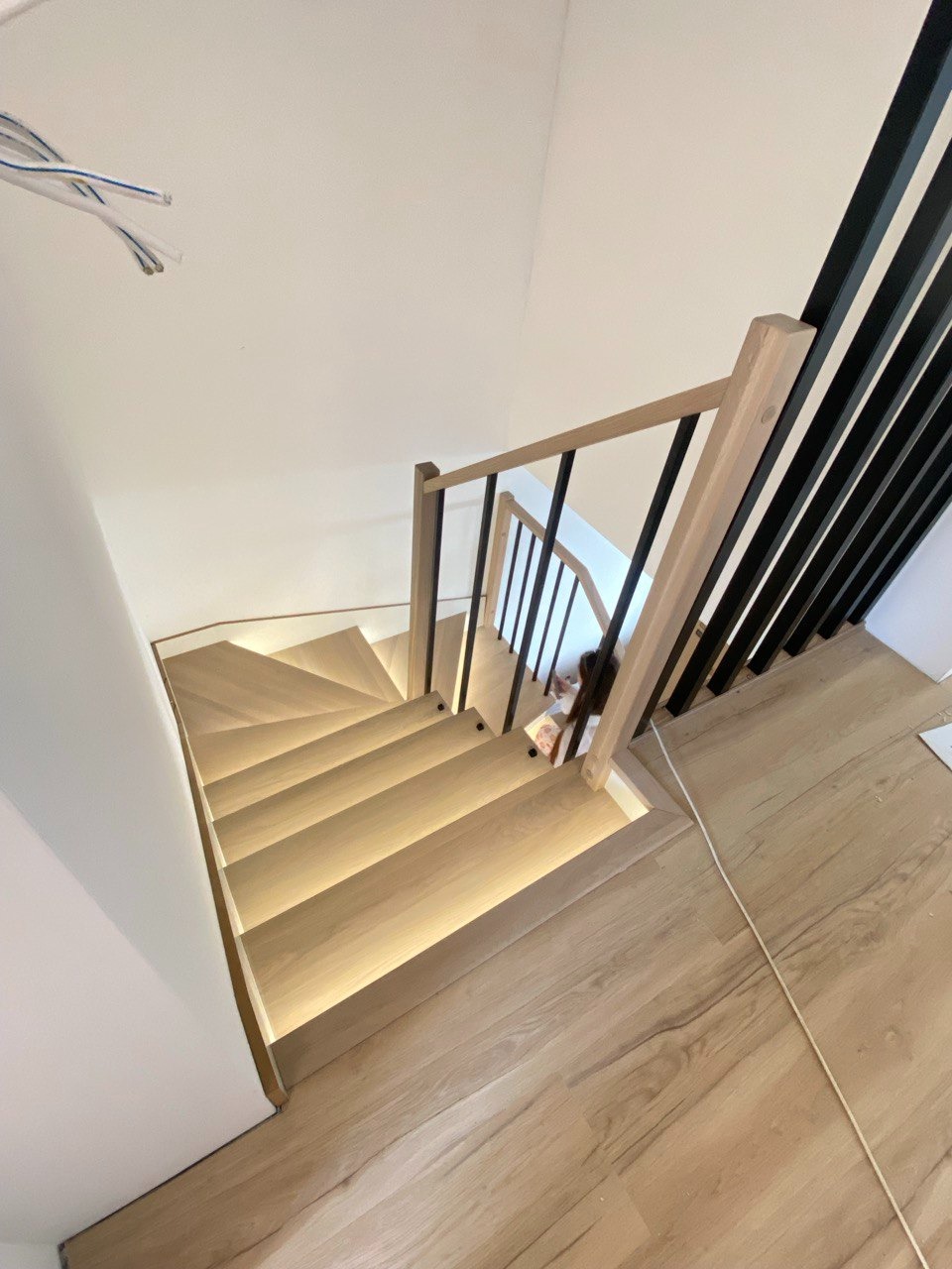 Nowoczesne schody drewniane z podświetleniem LED i czarnymi balustradami, widok z góry, jasne drewno, minimalistyczny design, fragment podłogi.