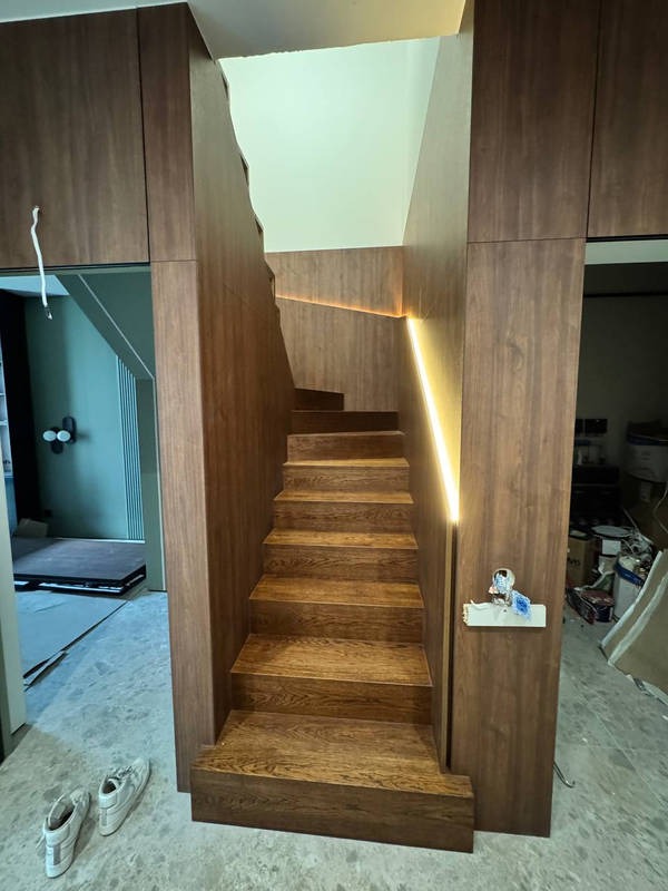 Nowoczesne schody z drewna w zabudowie, oświetlone listwą LED, z widocznymi butami na podłodze i elementami wyposażenia w tle.