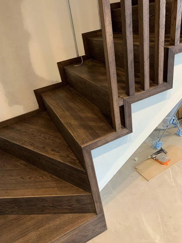 Nowoczesne schody z ciemnego drewna z minimalistyczną balustradą, widok z dołu, podkreślający detale wykończenia i fakturę drewna.