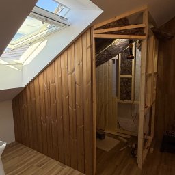 Timberhaus - Adaptacja poddasza: drewniana zabudowa skosu z oknem dachowym, widoczne ocieplenie i konstrukcja szkieletowa szafy wnękowej. Podłoga wyłożona panelami.