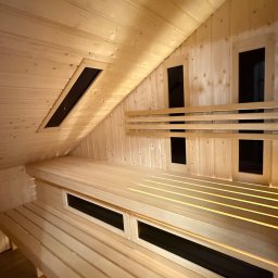 Timberhaus - Jasne drewno w saunie: ławy, ściany i sufit z oknami wentylacyjnymi. Ukośny sufit i ciepłe oświetlenie tworzą relaksującą atmosferę.
