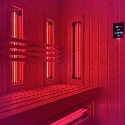 Timberhaus - Wnętrze sauny infrared z drewnianą ławą i panelami grzewczymi, oświetlone intensywnym czerwonym światłem. Widoczny panel sterowania na ścianie.
