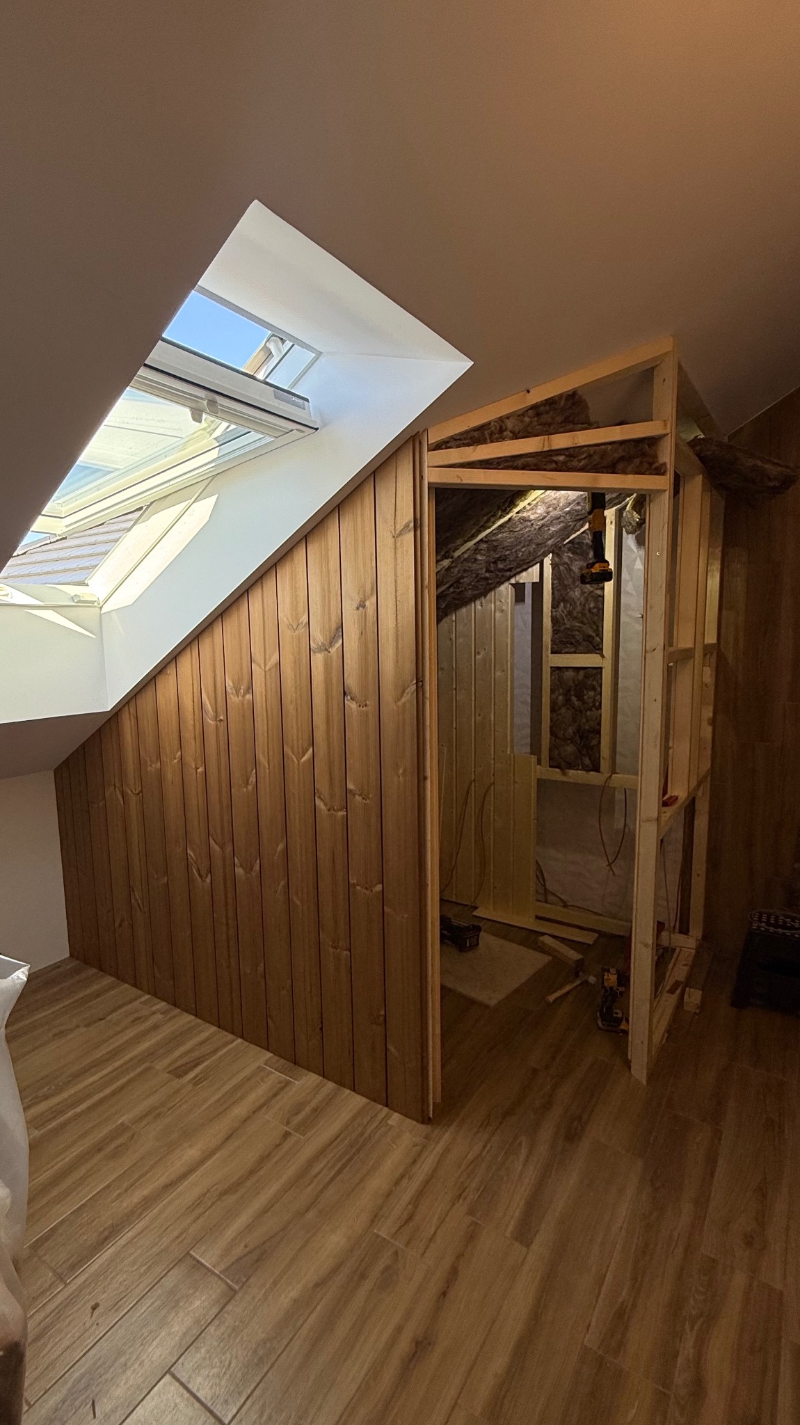Adaptacja poddasza: drewniana zabudowa skosu z oknem dachowym, widoczne ocieplenie i konstrukcja szkieletowa szafy wnękowej. Podłoga wyłożona panelami.