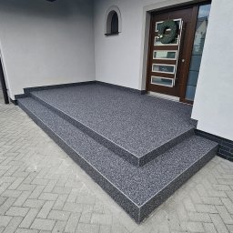 Dorbudex Paweł Dorabiała - Wykończone żywicą schody wejściowe do domu z ciemnymi drzwiami i wieńcem. Nowoczesna aranżacja z szarą posadzką żywiczną na zewnątrz budynku.