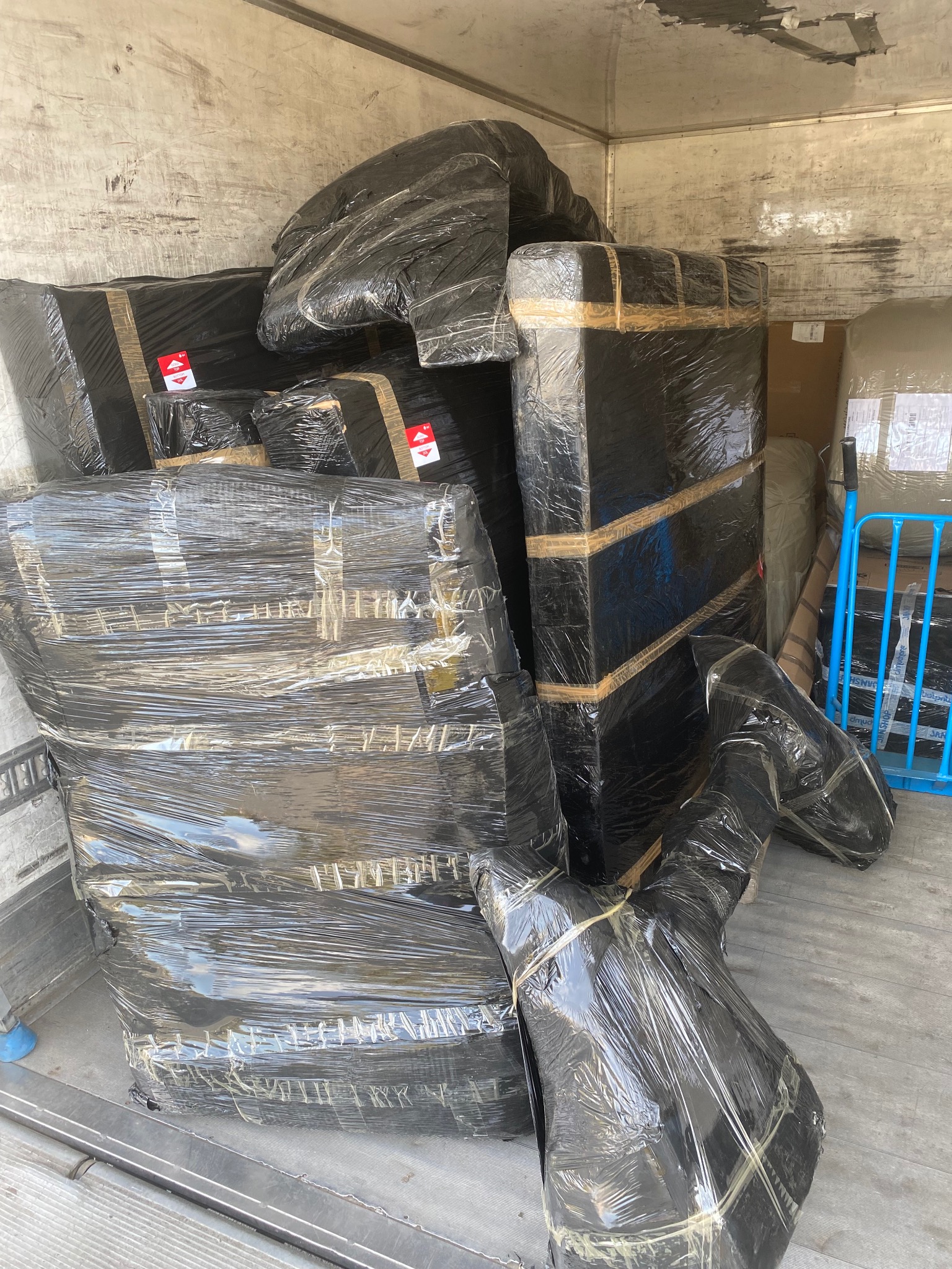 Ładunek zabezpieczony folią i taśmą w przestrzeni ładunkowej pojazdu. Widoczne kartony i elementy owinięte folią stretch.