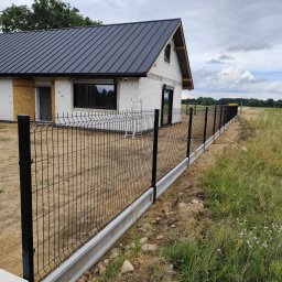 Clean Service &Garden Roman Zalewski - Nowoczesne ogrodzenie panelowe w kolorze czarnym z podmurówką betonową, na tle domu w trakcie budowy i zielonego krajobrazu. Widok z perspektywy.
