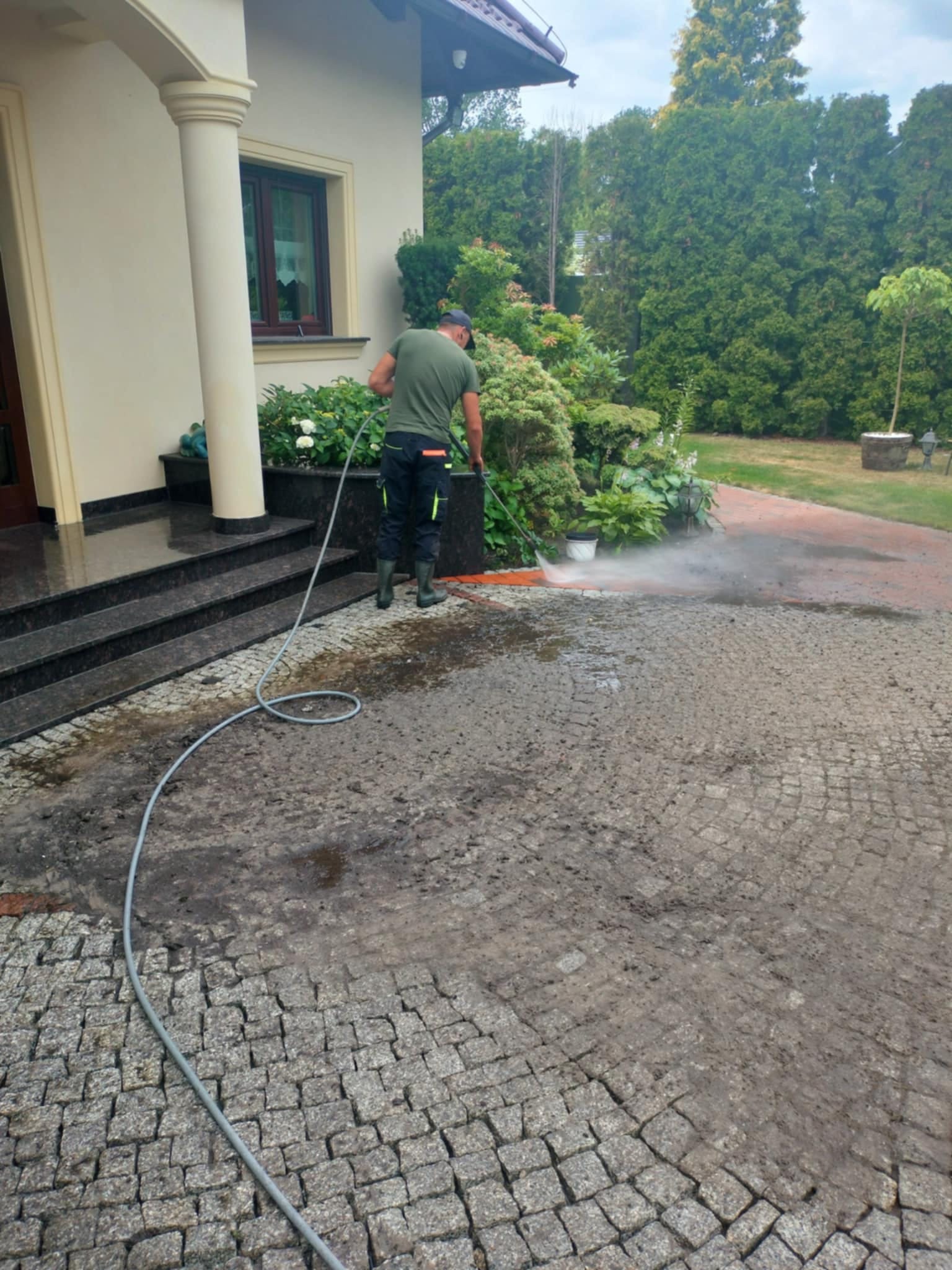 Czyszczenie kostki brukowej przy domu jednorodzinnym za pomocą myjki ciśnieniowej. Widoczny fragment chodnika przed i po czyszczeniu.