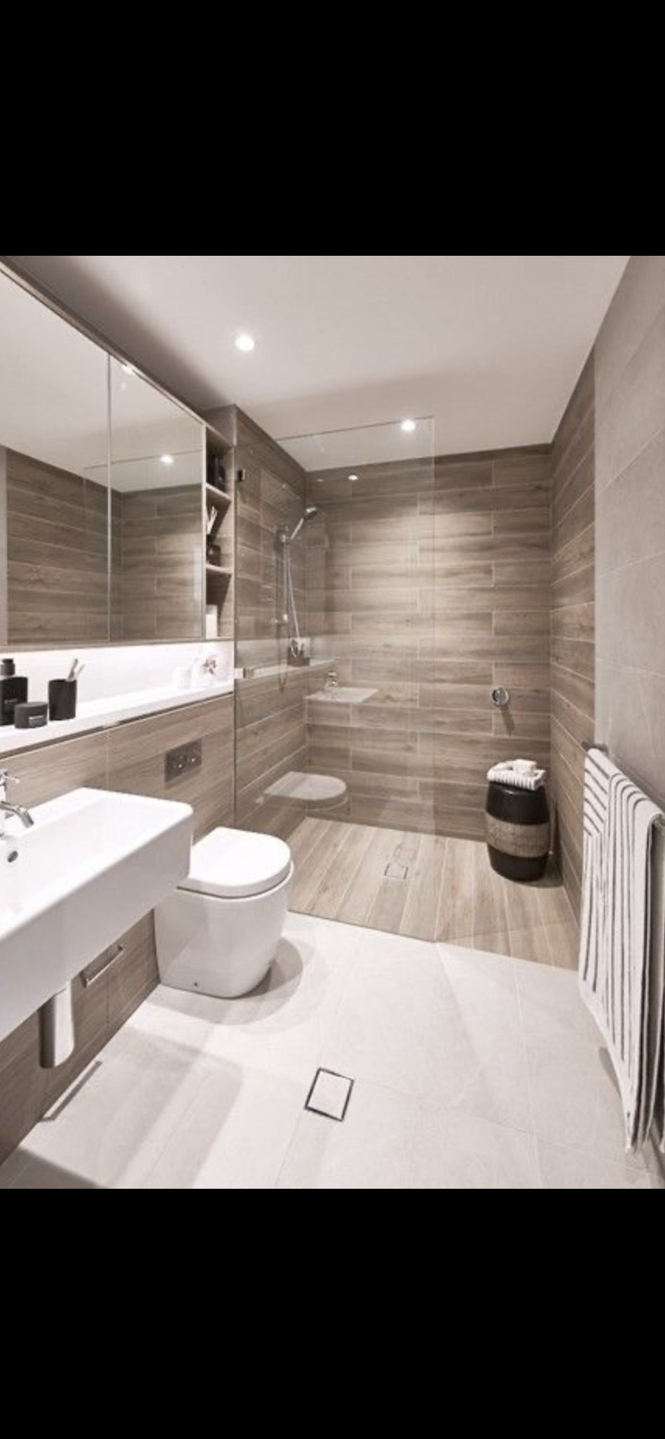 Nowoczesna łazienka z kabiną typu walk-in, wykończona płytkami imitującymi drewno, minimalistyczna umywalka i toaleta, oświetlenie punktowe.