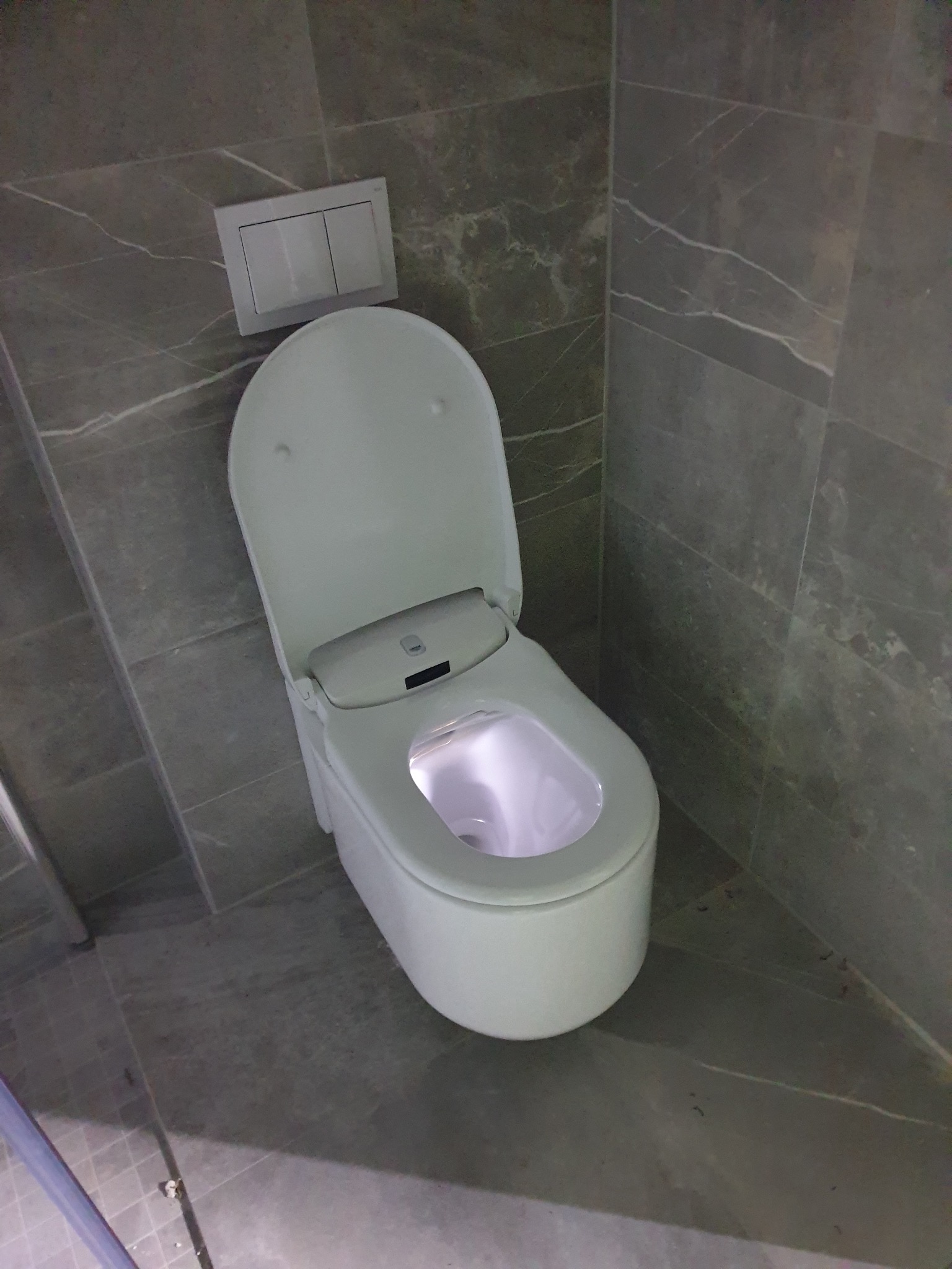 Nowoczesna toaleta z podświetleniem LED w wykończonej łazience, szare płytki imitujące marmur na ścianach i podłodze. Uwagę zwraca podświetlona misa.