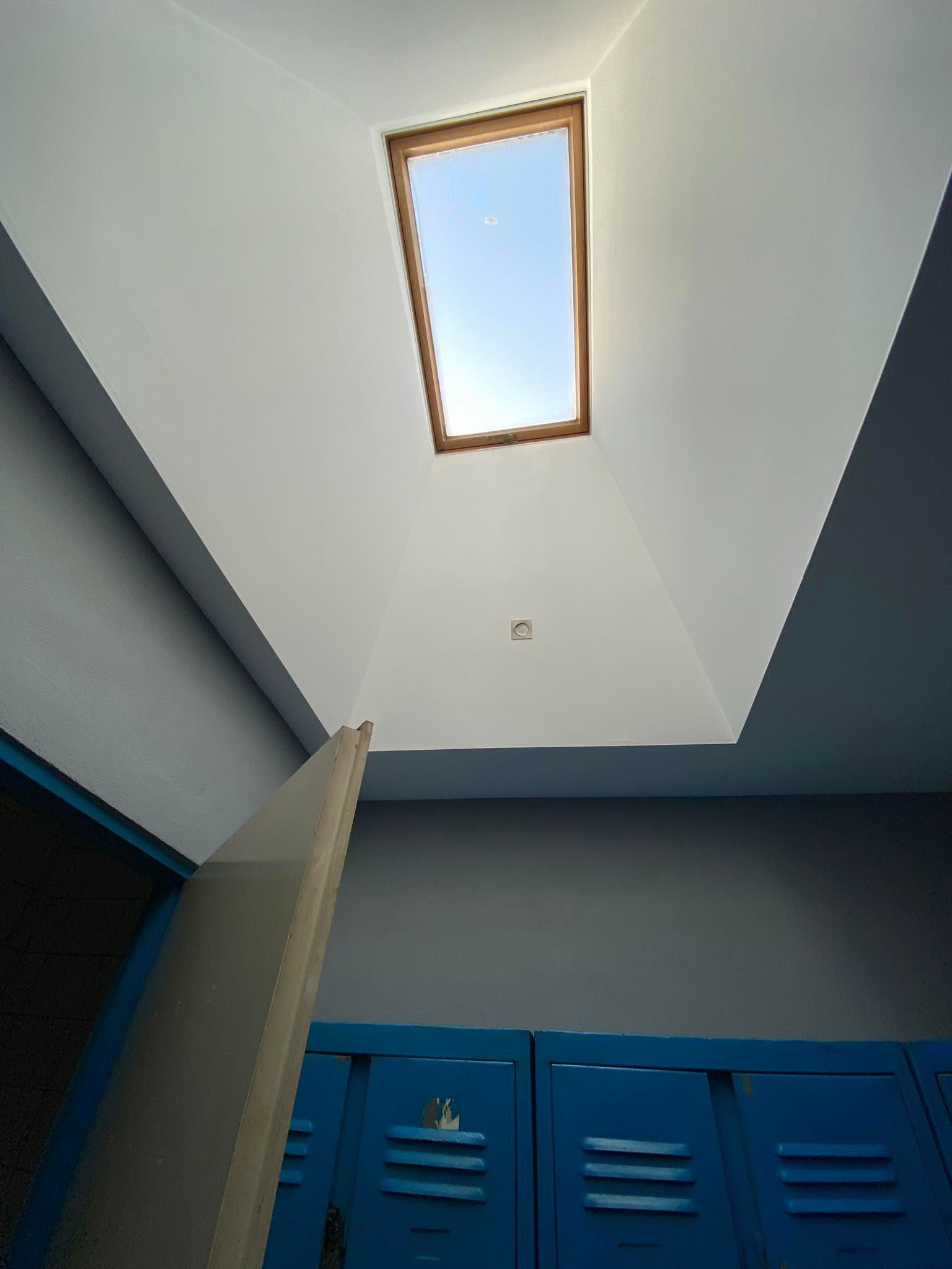 Pomieszczenie po malowaniu: biały sufit z oknem dachowym i szare ściany nad niebieskimi szafkami. Widoczna krawędź płyty gipsowej.